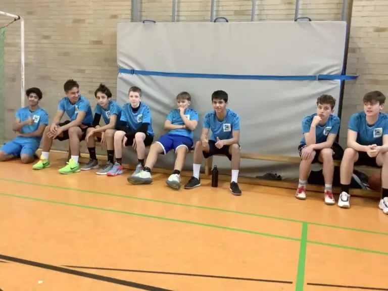 Schülermannschaft in blauen Trikots sitzt auf einer Bank in der Sporthalle