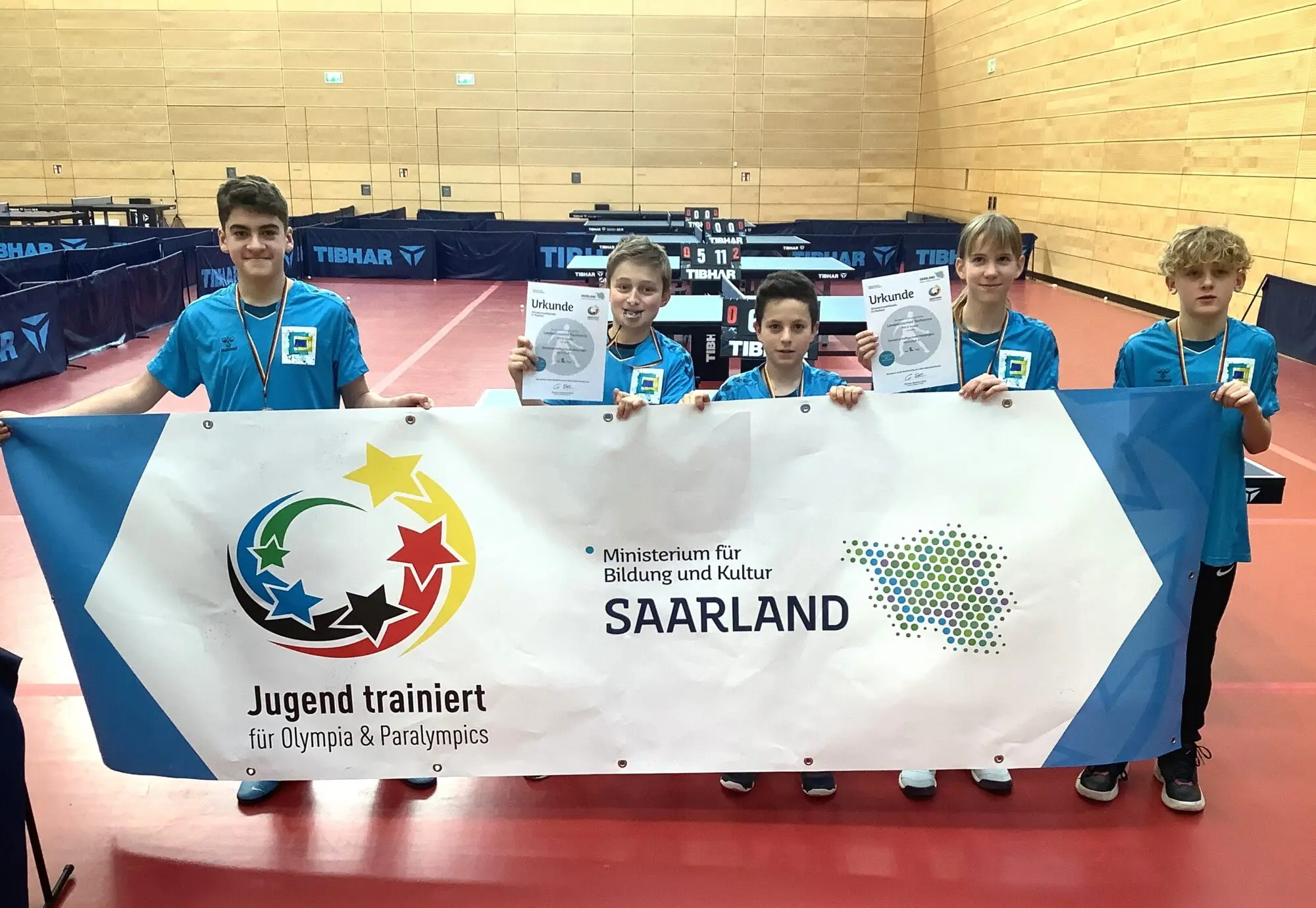 Schüler in blauen Shirts halten ein Banner „Jugend trainiert für Olympia & Paralympics – Saarland“