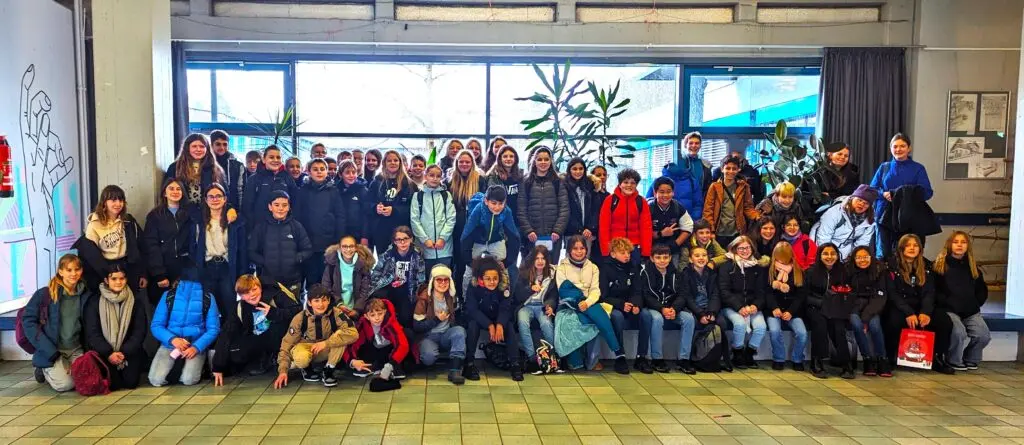 Große Gruppe von Schülerinnen und Schülern sitzt und steht für ein Gruppenfoto in einer Halle
