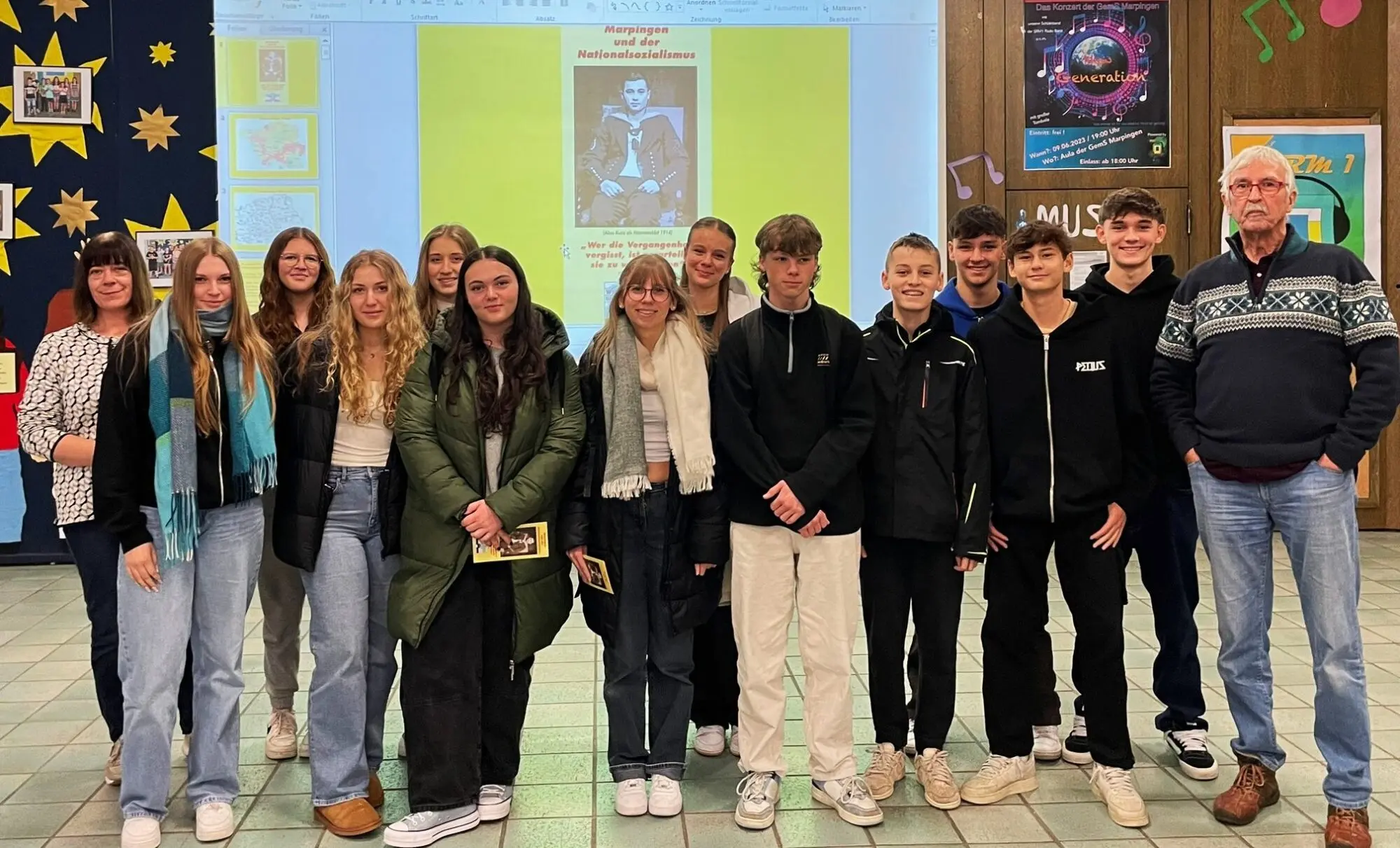 Gruppe von Jugendlichen und Erwachsenen posiert in der Aula vor einer Projektionswand