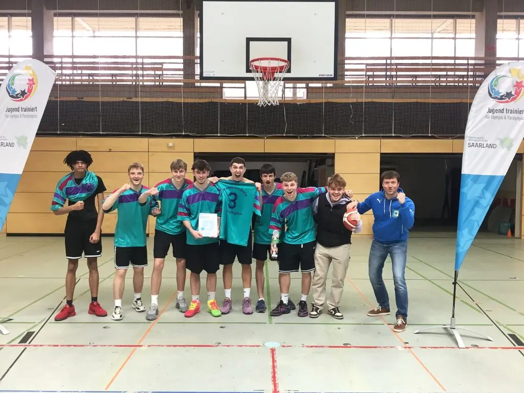 Schülermannschaft in grünen Trikots steht in einer Sporthalle neben Werbebannern
