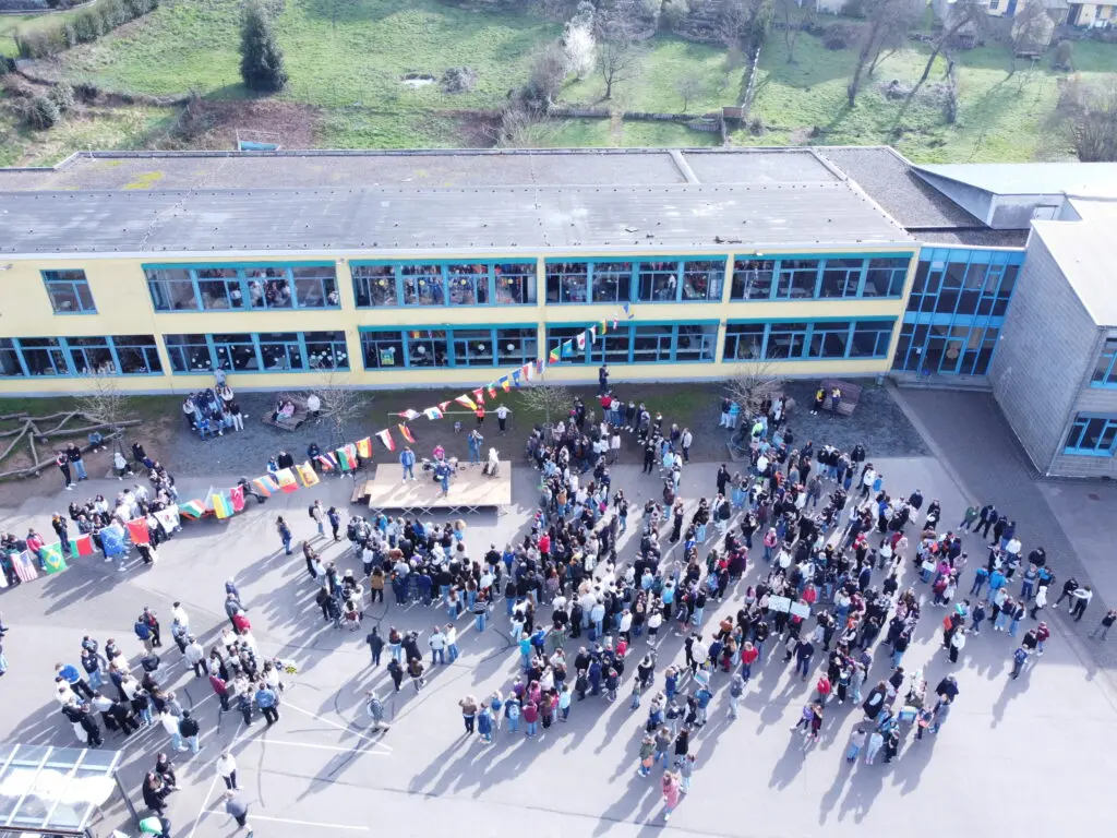 Drohnenaufnahme der Schulgemeinschaft, die sich auf dem Schulhof vor dem Gebäude versammelt