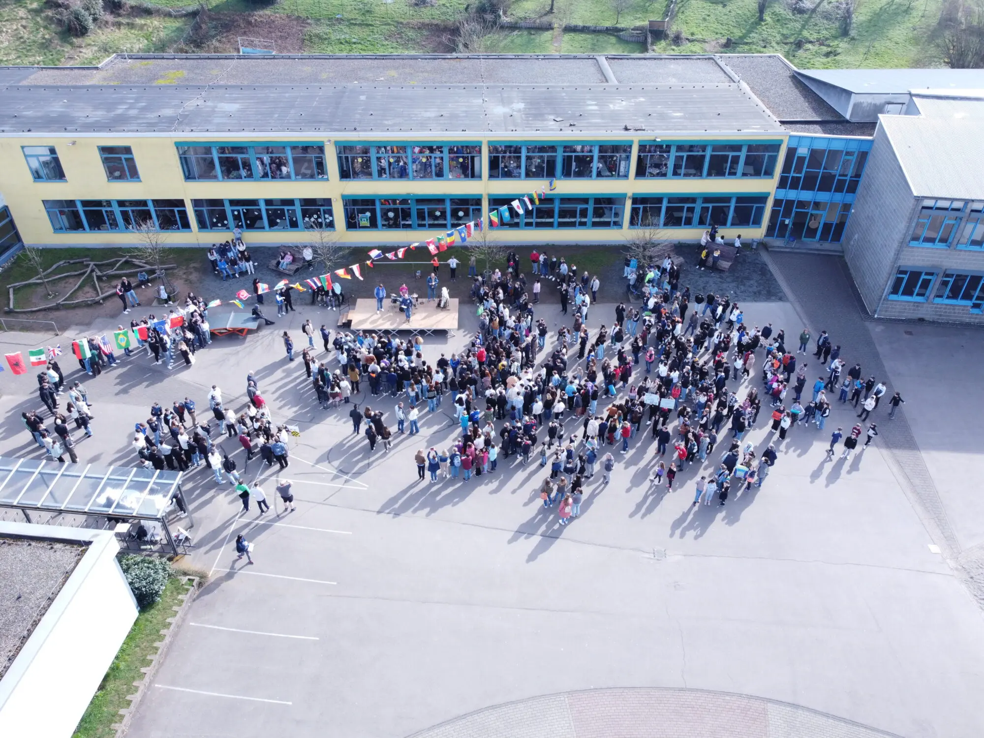 Luftbild des Schulhofs mit großer Menschenmenge vor dem Schulgebäude