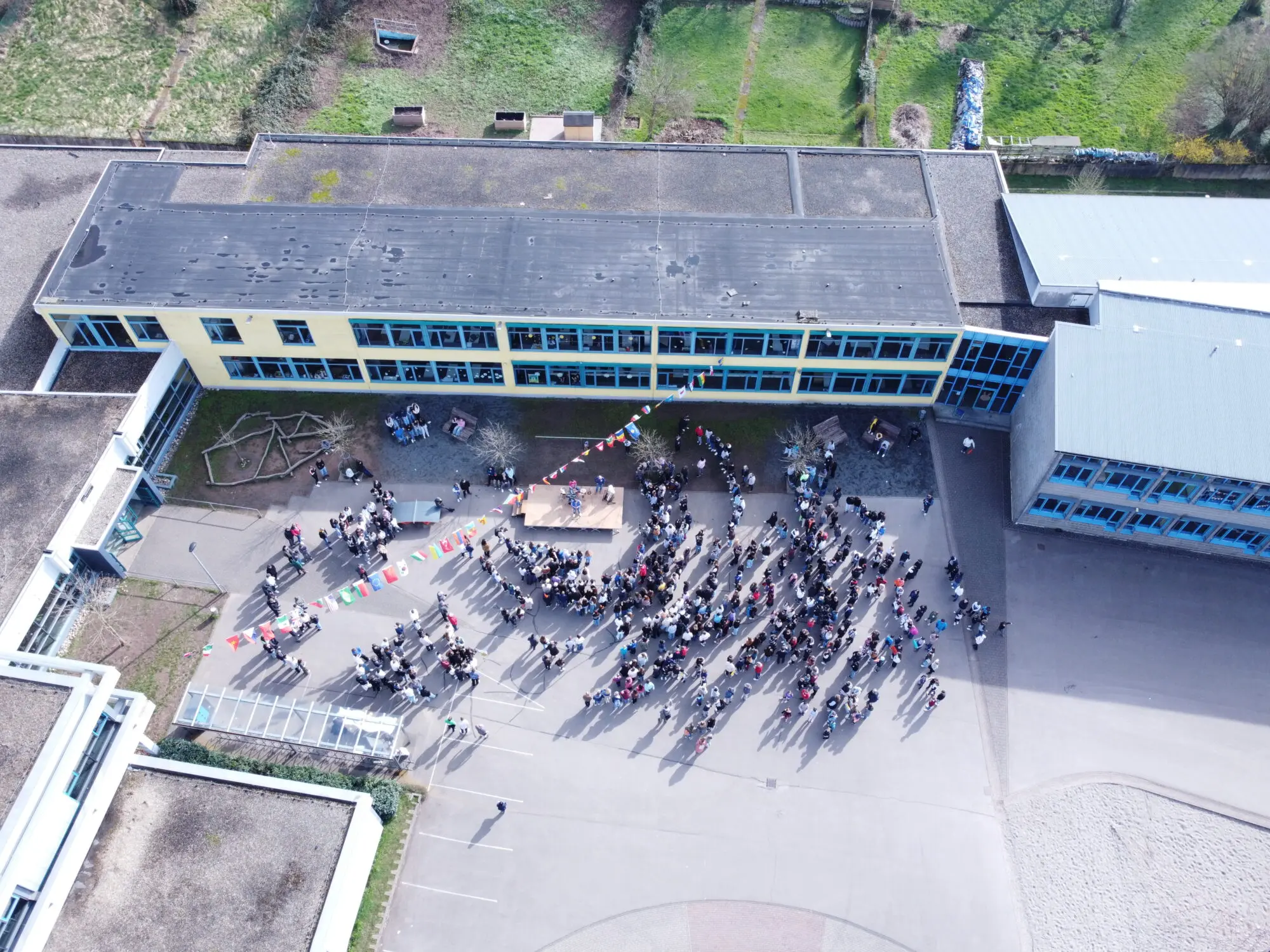 Drohnenaufnahme des Schulgeländes mit versammelten Schülerinnen und Schülern auf dem Hof