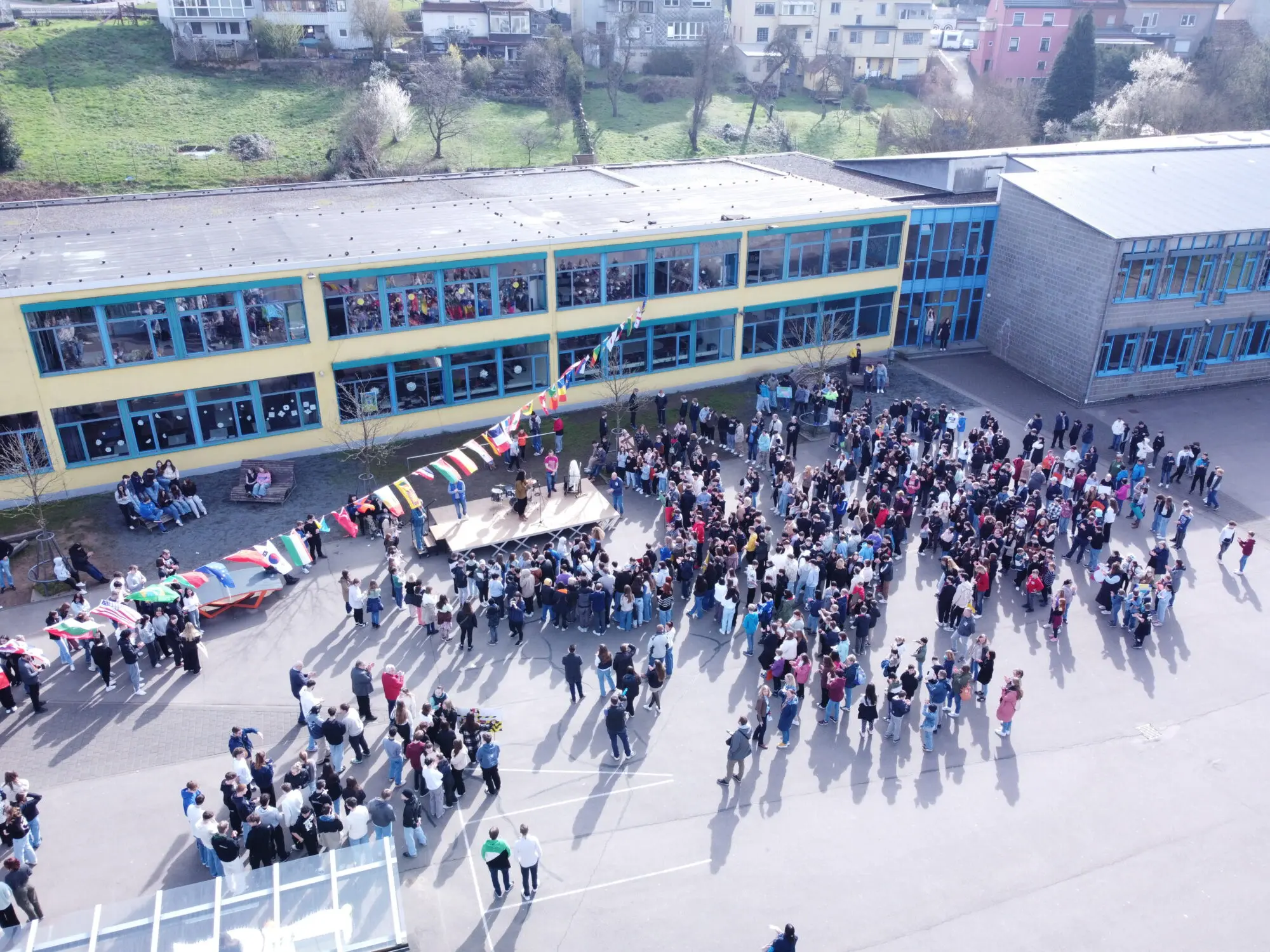 Luftaufnahme: Schülerinnen und Schüler versammeln sich in Gruppen auf dem Schulhof