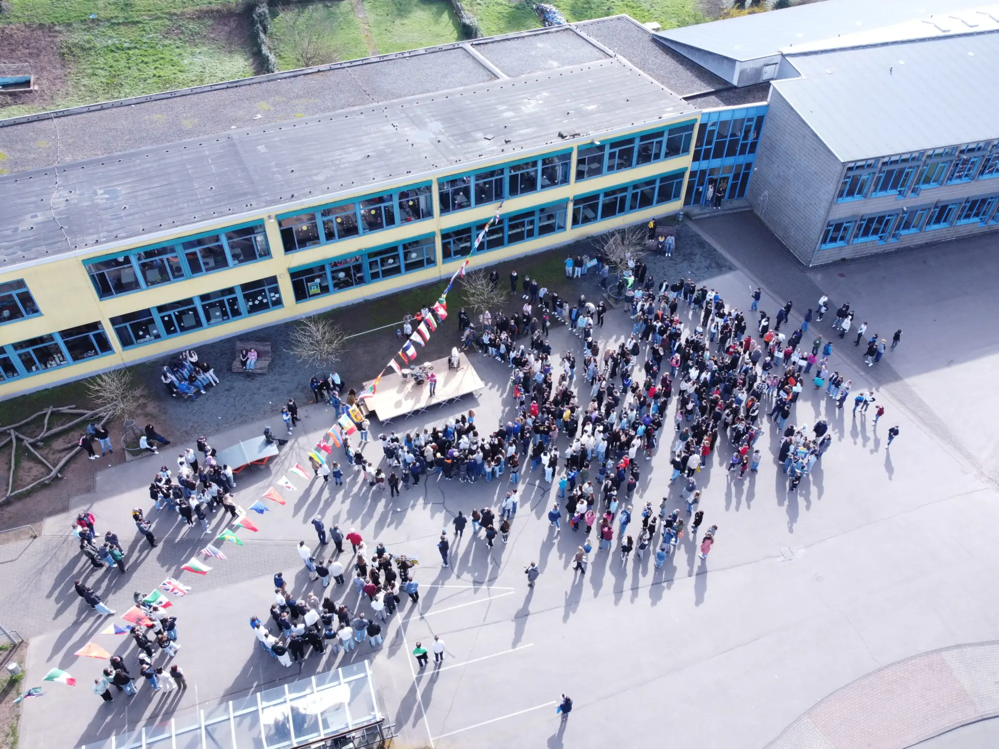 Drohnenbild der Schulgemeinschaft auf dem Schulhof vor dem langgestreckten Schulgebäude