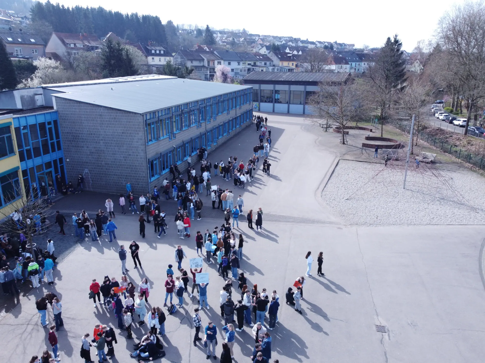 Drohnenaufnahme einer langen Menschenkette, die sich über den Schulhof zieht