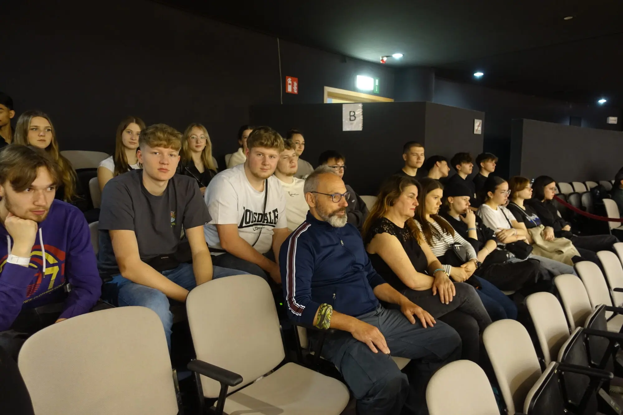 Schülergruppe sitzt in einem abgedunkelten Vortragssaal auf Stuhlreihen