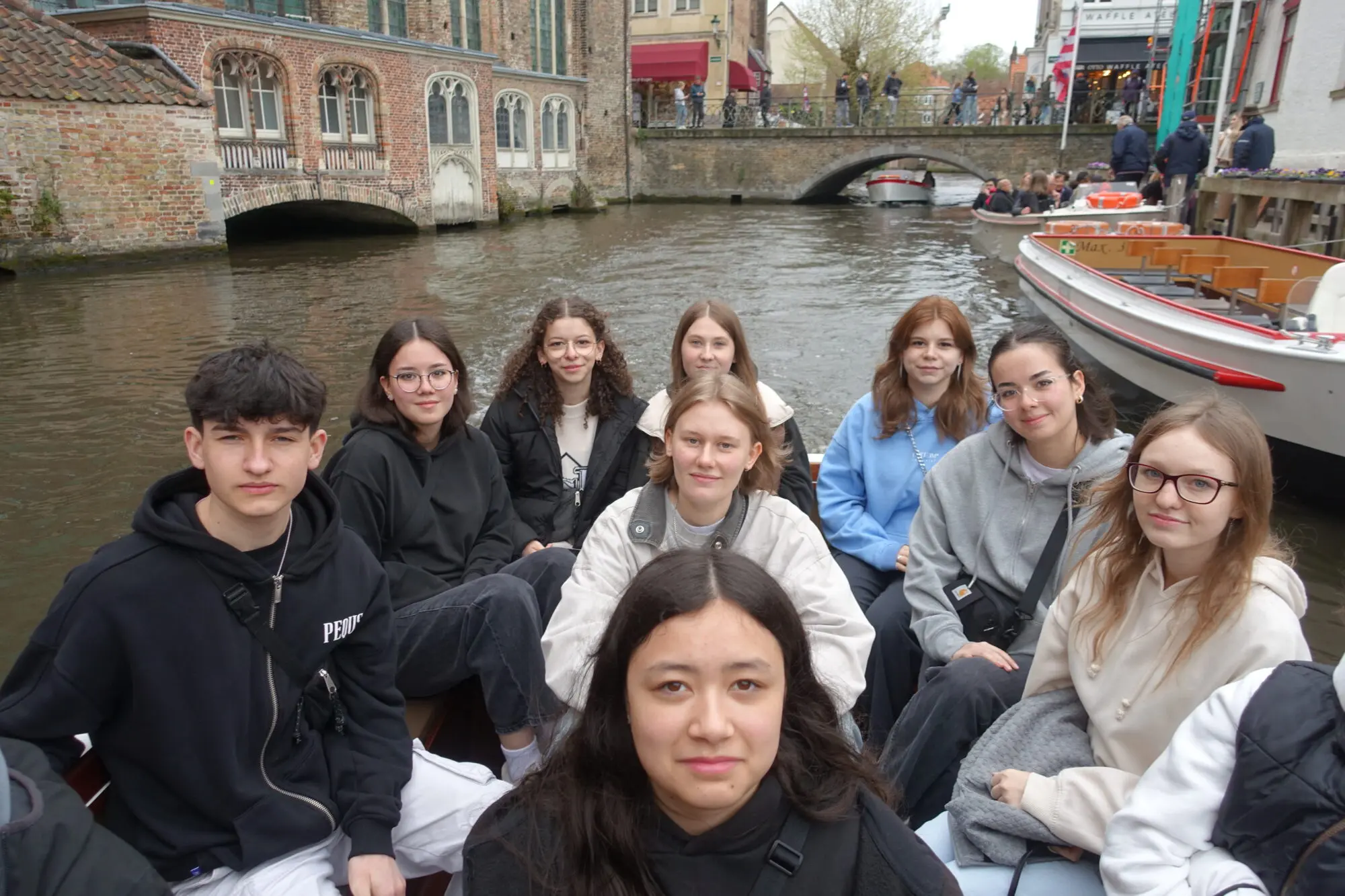 Schülerinnen und Schüler sitzen in einem Boot auf einem Kanal, im Hintergrund Altstadthäuser