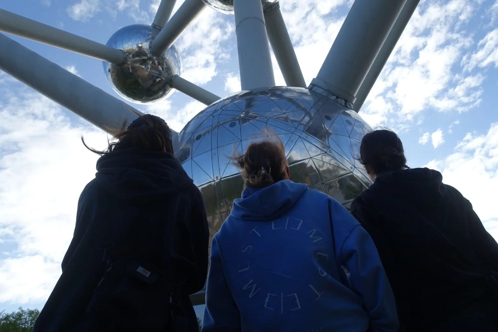 Drei Jugendliche von hinten vor den glänzenden Kugeln des Atomiums