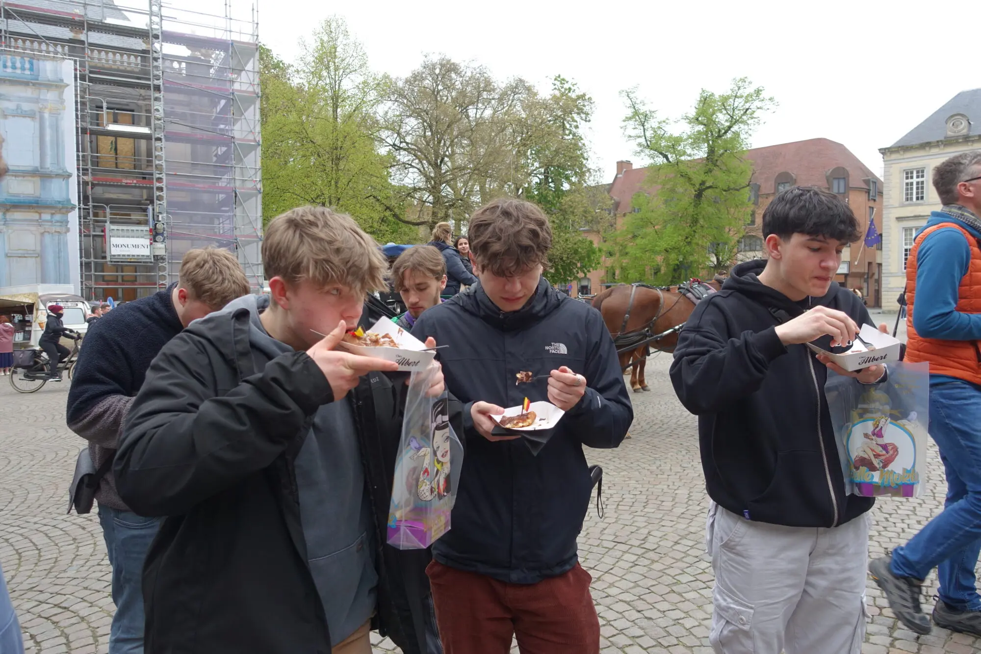 Jugendliche essen auf einem Platz in der Altstadt Snacks aus Papiertüten