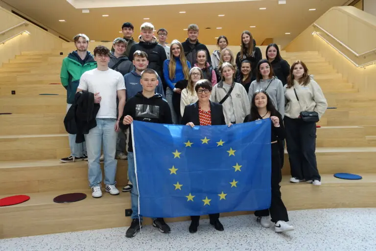 Schülergruppe mit Europafahne auf Sitzstufen in einem modernen Gebäude