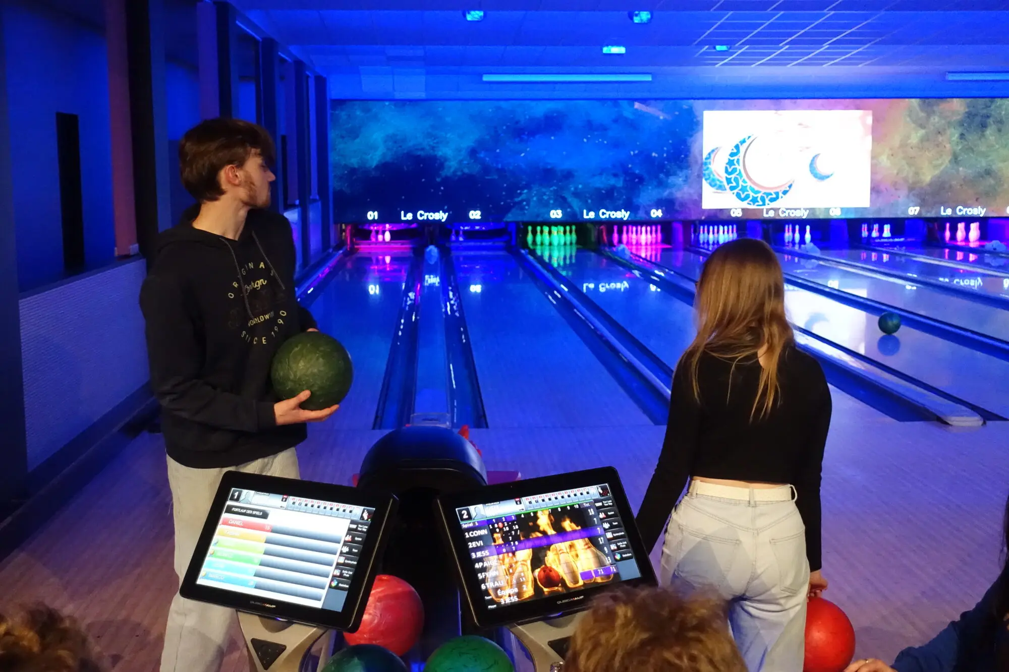Jugendliche beim Bowling auf einer bunt beleuchteten Bowlingbahn mit Anzeigebildschirmen