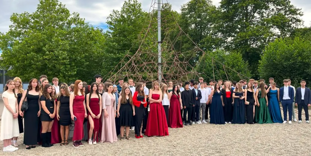 Abschlussjahrgang in festlicher Kleidung als Gruppe im Freien vor Bäumen