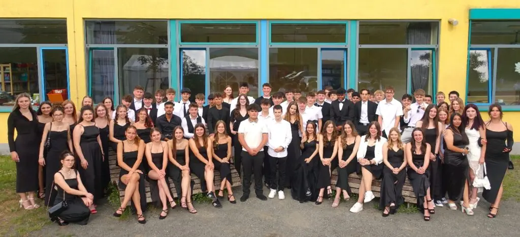 Abschlussjahrgang in festlicher Kleidung als Gruppe vor dem Schulgebäude