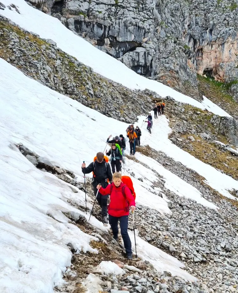 Wandergruppe steigt einen steilen, teils verschneiten Bergpfad hinauf