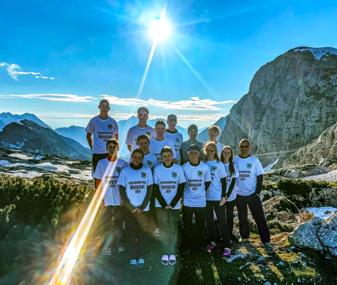 Wandergruppe in weißen T-Shirts steht vor Berggipfeln im strahlenden Sonnenlicht