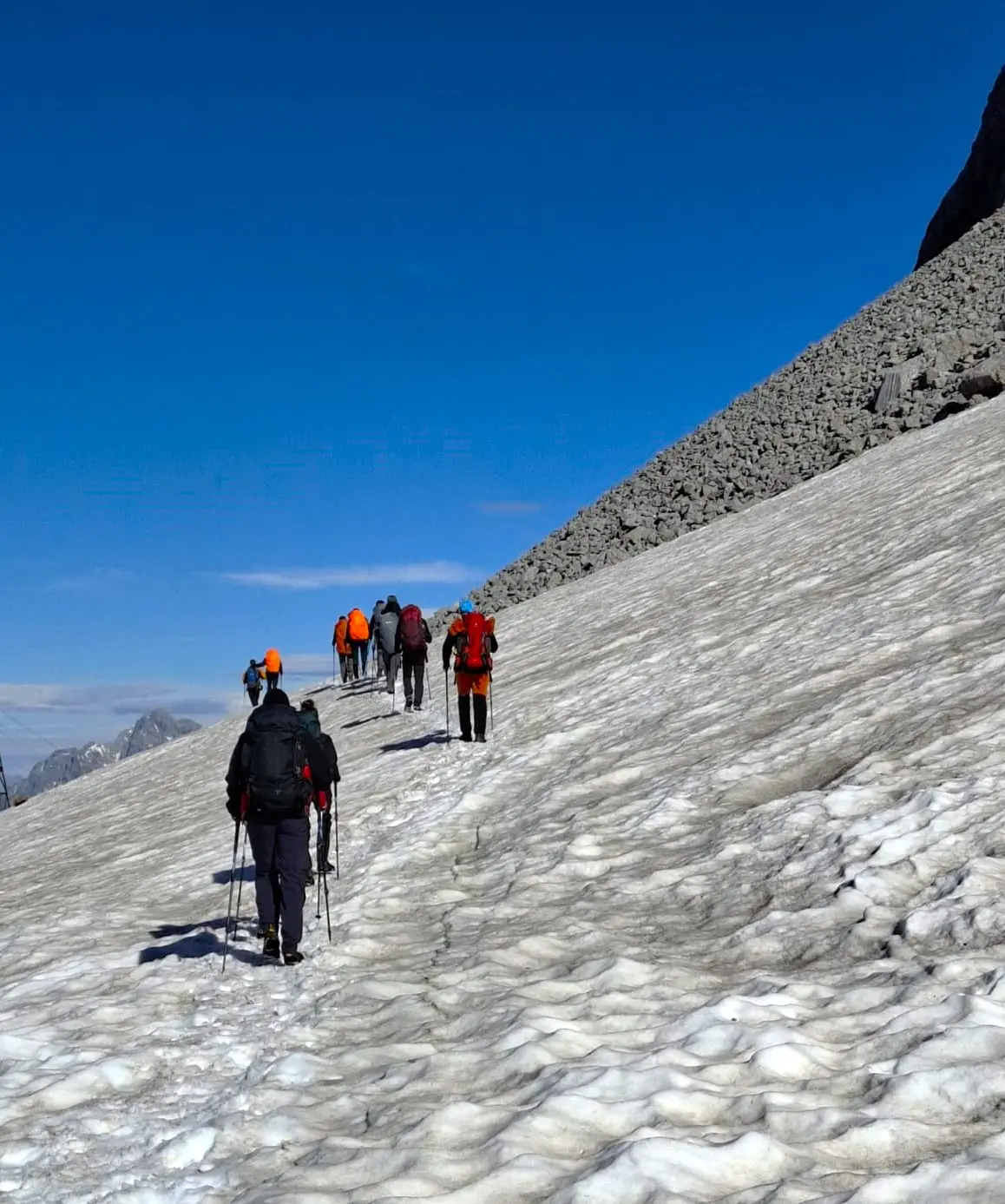 Wandernde steigen über ein steiles Schneefeld im Hochgebirge vor blauem Himmel