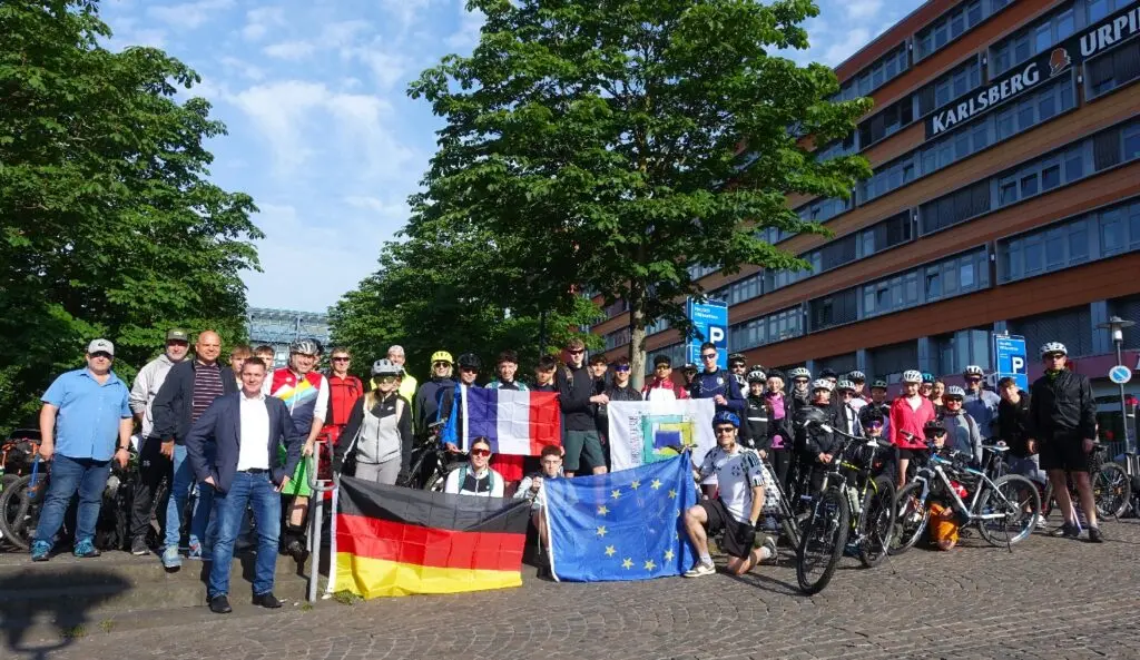 Gruppe mit Fahrrädern sowie Deutschland- und Europafahne vor einem Gebäude