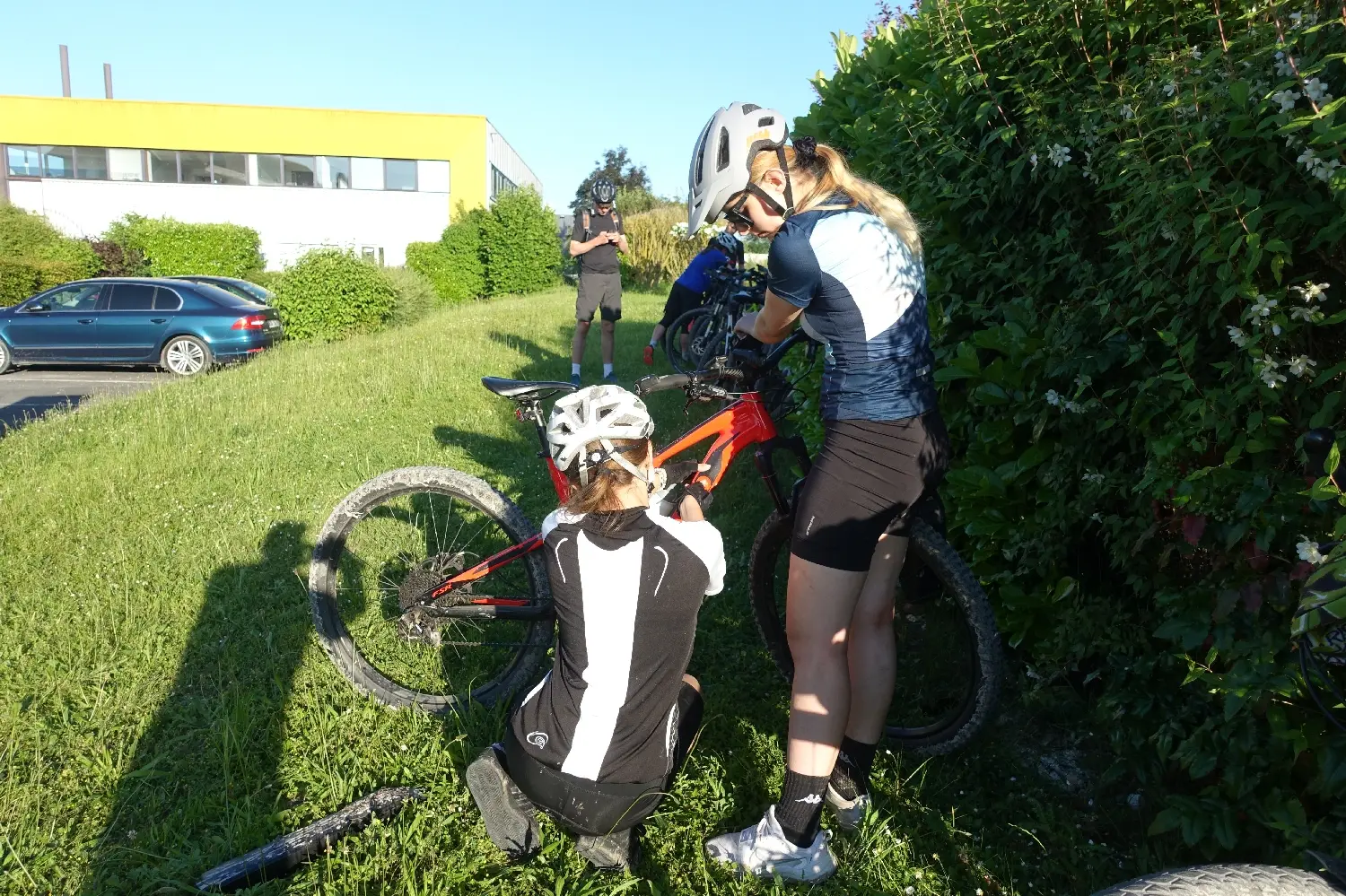 Zwei Radfahrende mit Helmen machen Pause mit ihren Rädern am grünen Wegrand