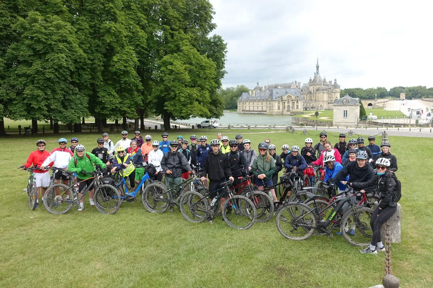 Radfahrergruppe mit Fahrrädern auf einer Wiese, im Hintergrund ein Schloss