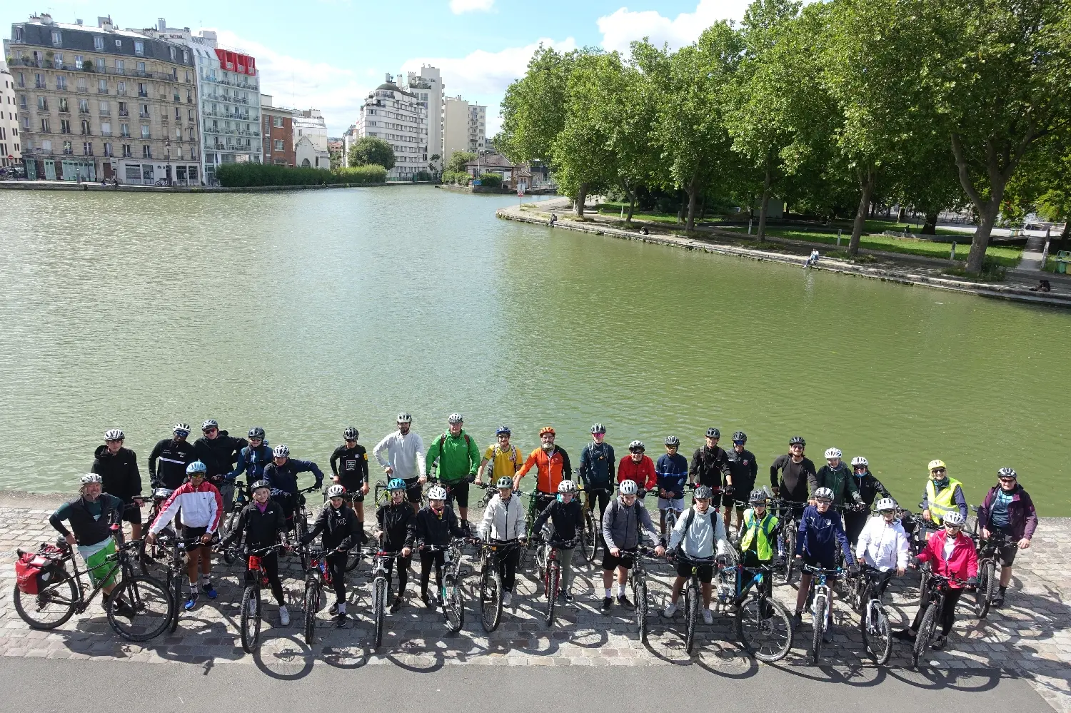 Radfahrergruppe mit Fahrrädern vor einem großen Wasserbecken in einer Stadt
