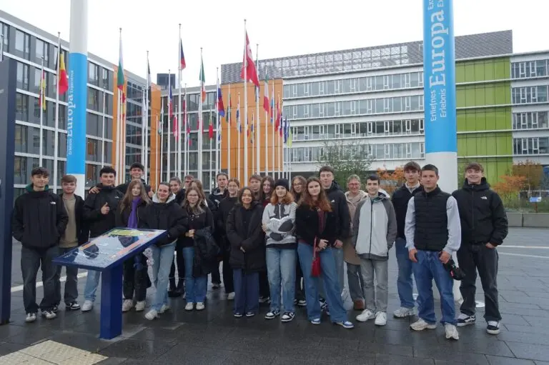 Schülergruppe vor einem modernen Gebäude mit Fahnen und Infotafel