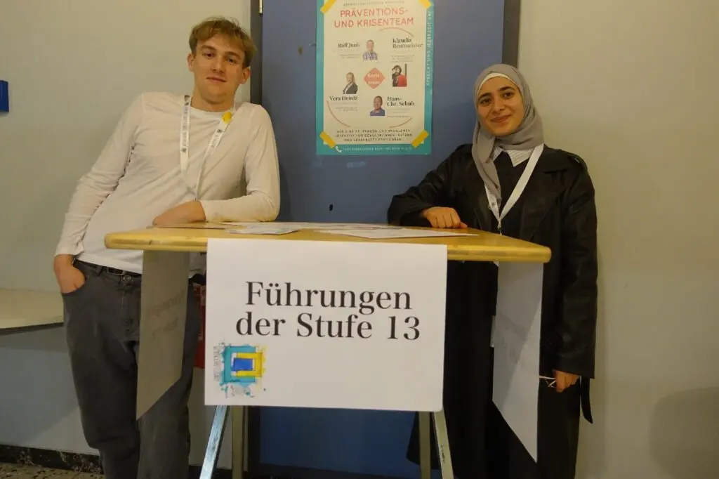 Zwei Schülerinnen stehen an einem Tisch mit dem Schild „Führungen der Stufe 13“