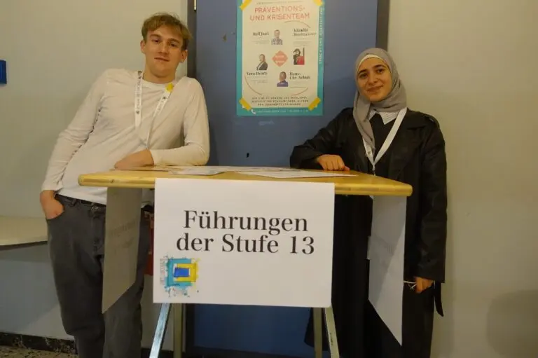 Zwei Schülerinnen stehen an einem Tisch mit dem Schild „Führungen der Stufe 13“