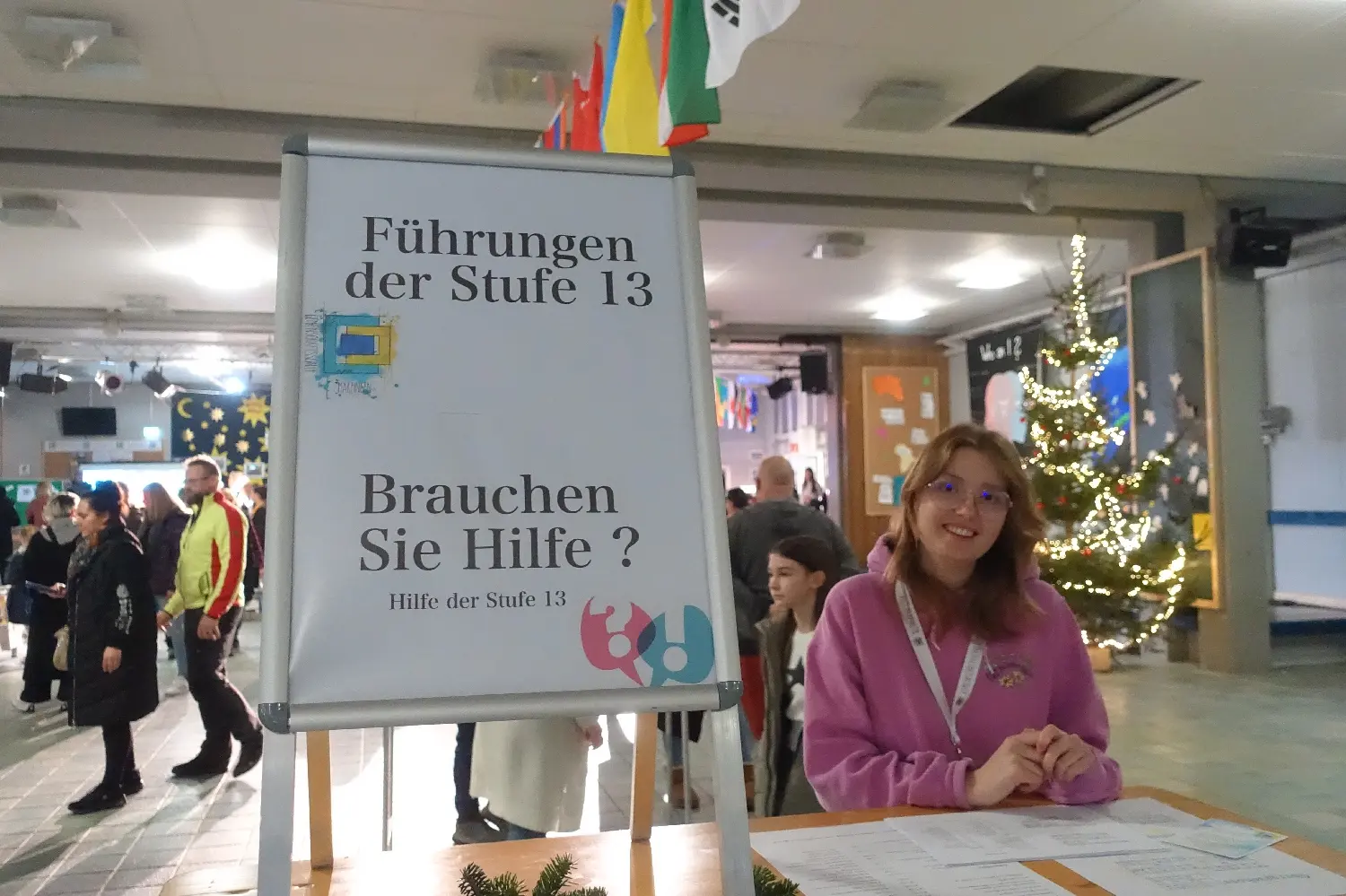 Schülerin an einem Tisch mit Schild „Führungen der Stufe 13 – Brauchen Sie Hilfe?“