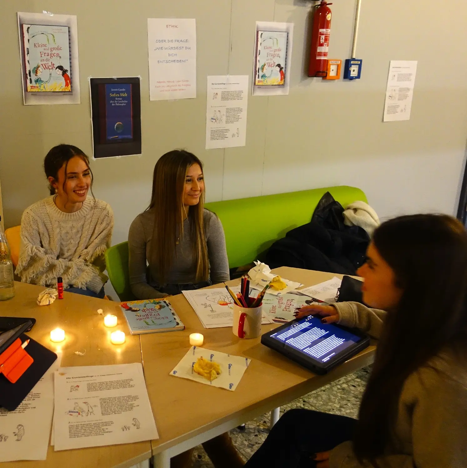 Schülerinnen und Kinder am Tisch mit Tablets und Kerzen bei einer Mitmachstation