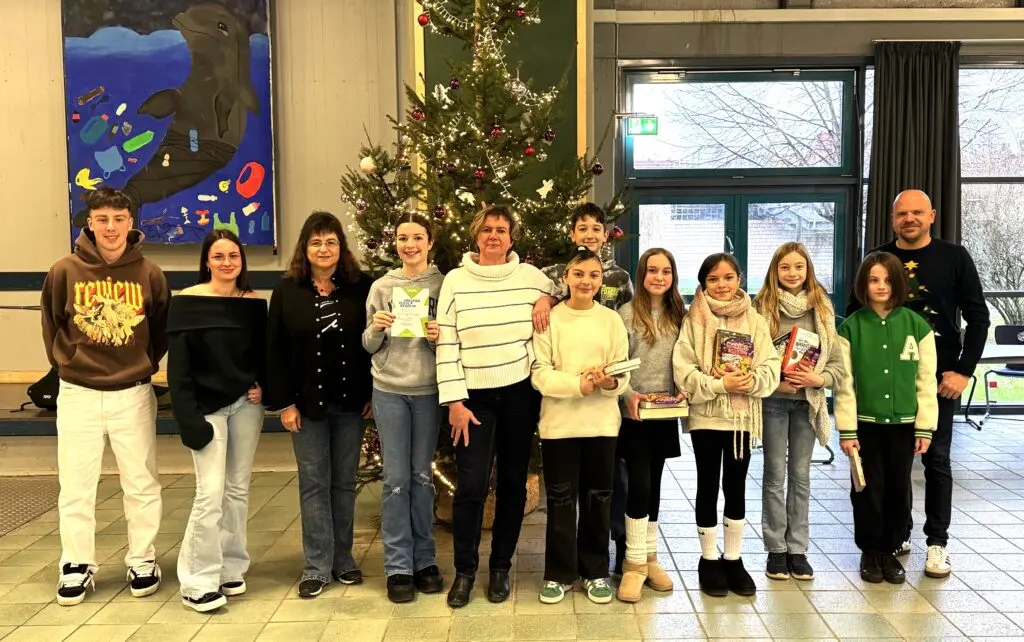 Gruppe von Schülerinnen, Schülern und Erwachsenen vor einem Weihnachtsbaum in der Schule