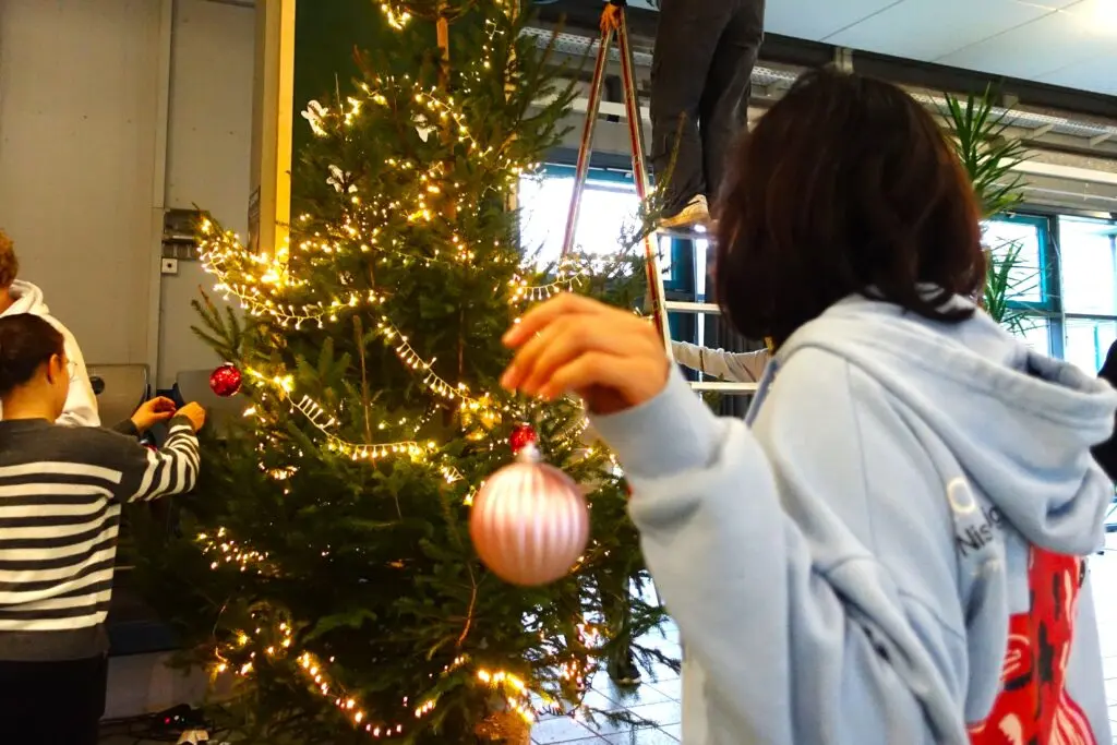 Jugendliche hängt eine Kugel an einen beleuchteten Weihnachtsbaum