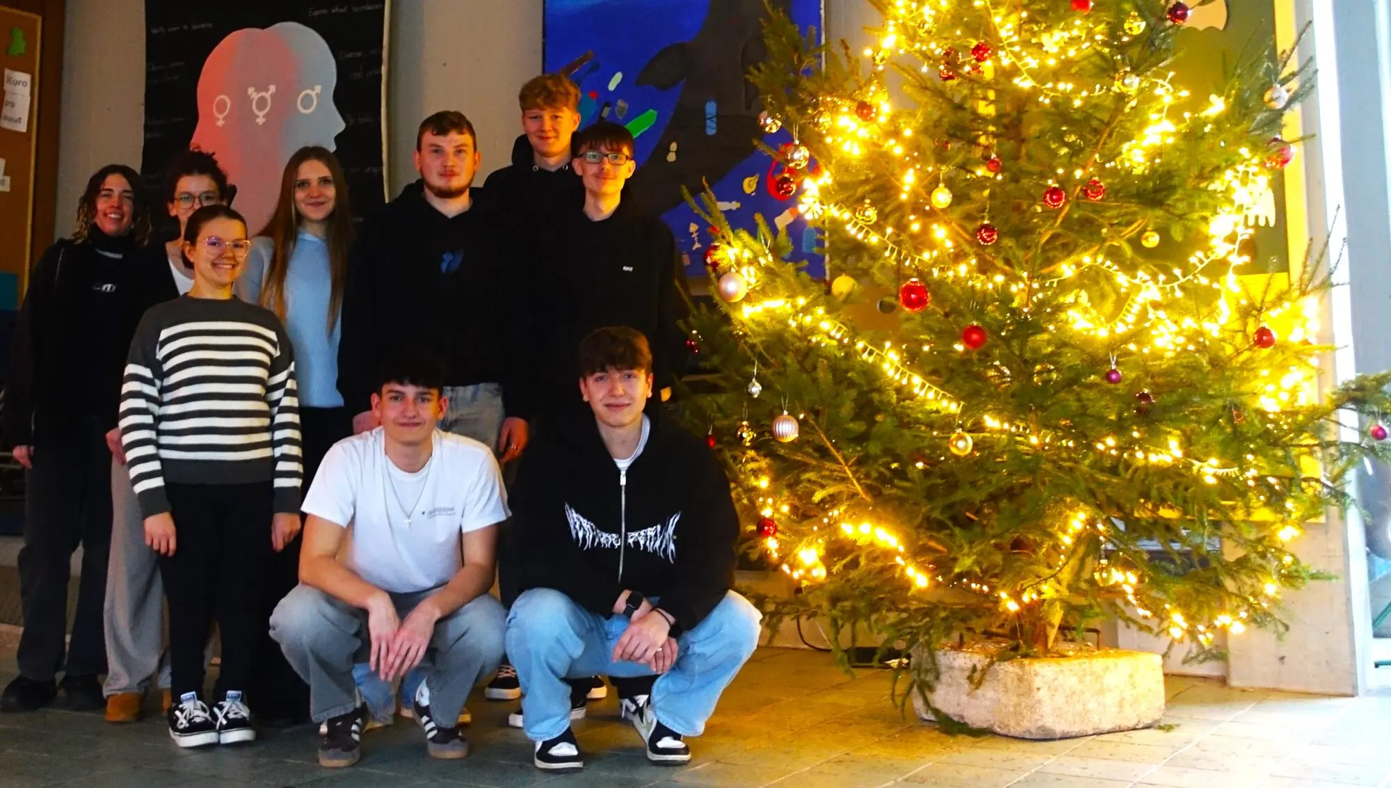 Schülergruppe posiert neben einem geschmückten, beleuchteten Weihnachtsbaum