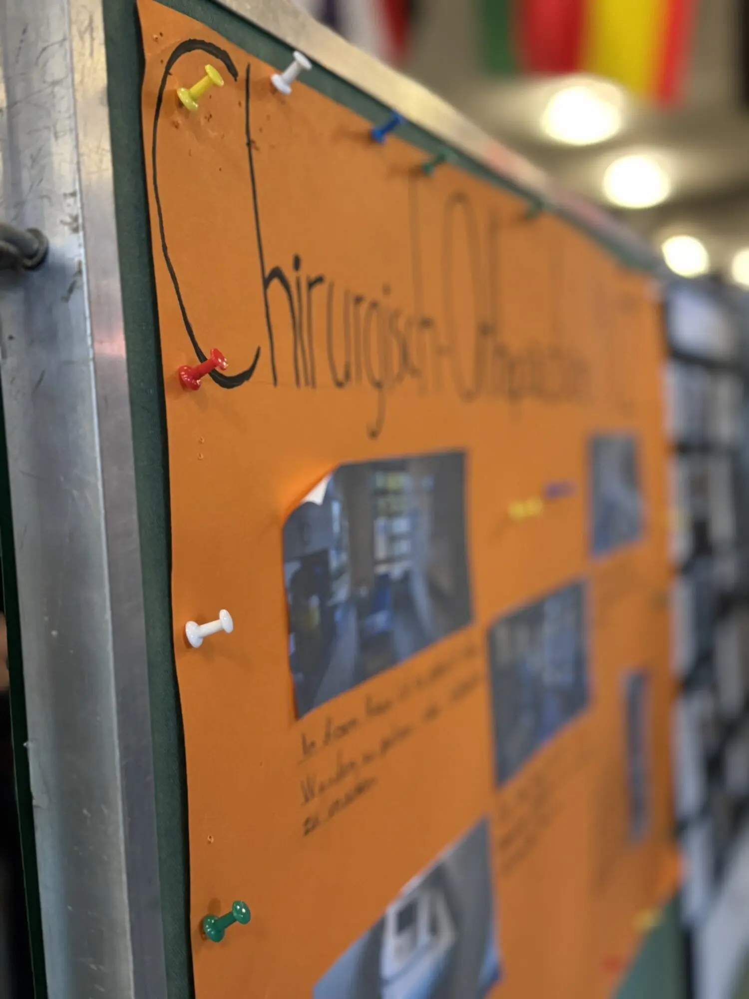 Orangefarbenes Plakat mit Fotos und Text an einer Stellwand, im Hintergrund Fahnengirlanden