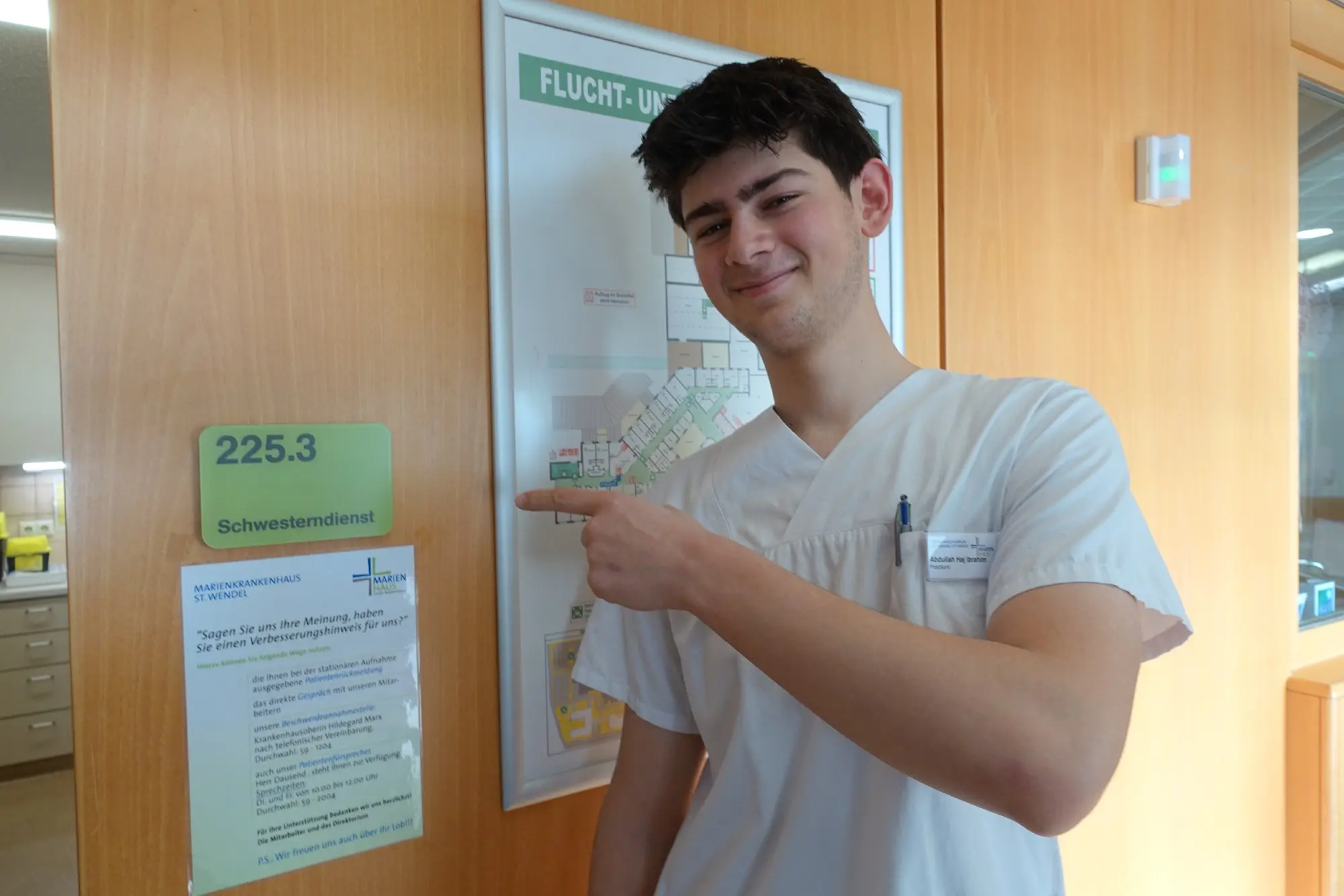 Junger Mann in weißer Kleidung zeigt auf einen Aushang an einer Wand