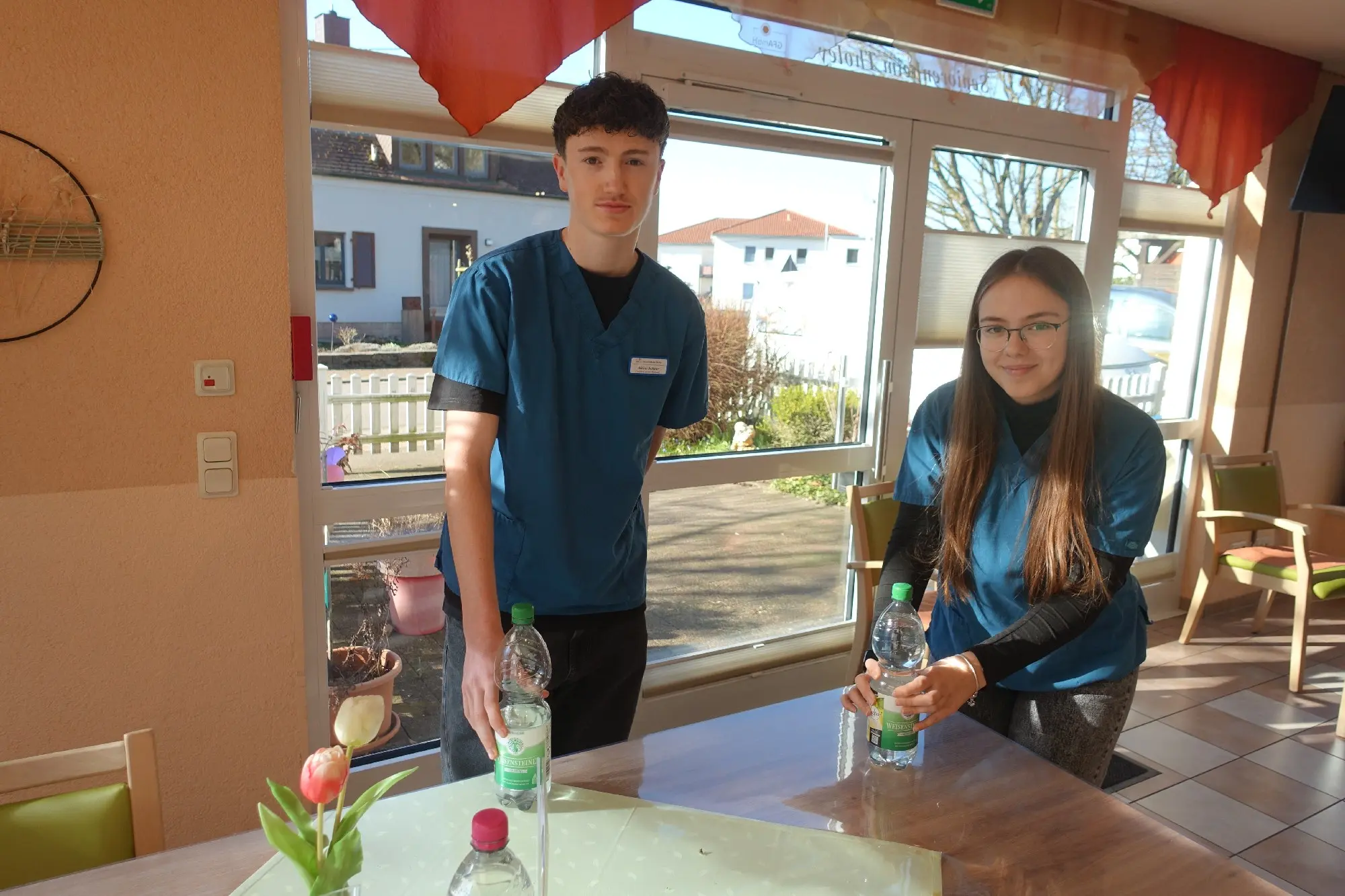 Junger Mann und Jugendliche an einem Tisch in einem hellen Aufenthaltsraum