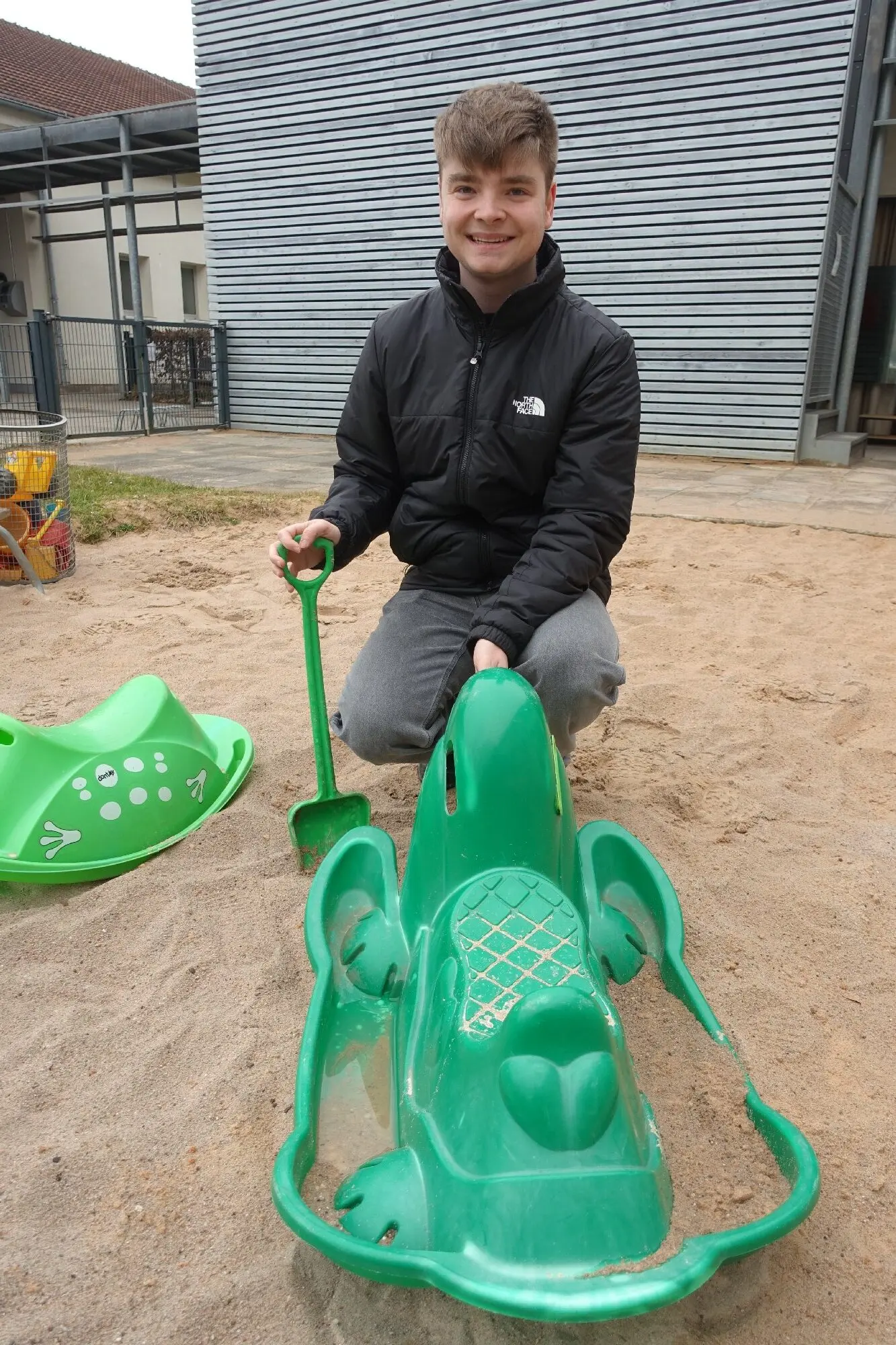 Jugendlicher sitzt auf einem grünen Spielgerät im Sandkasten