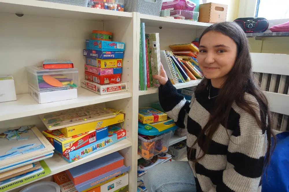 Junge Frau steht vor einem Regal mit Gesellschaftsspielen und Büchern