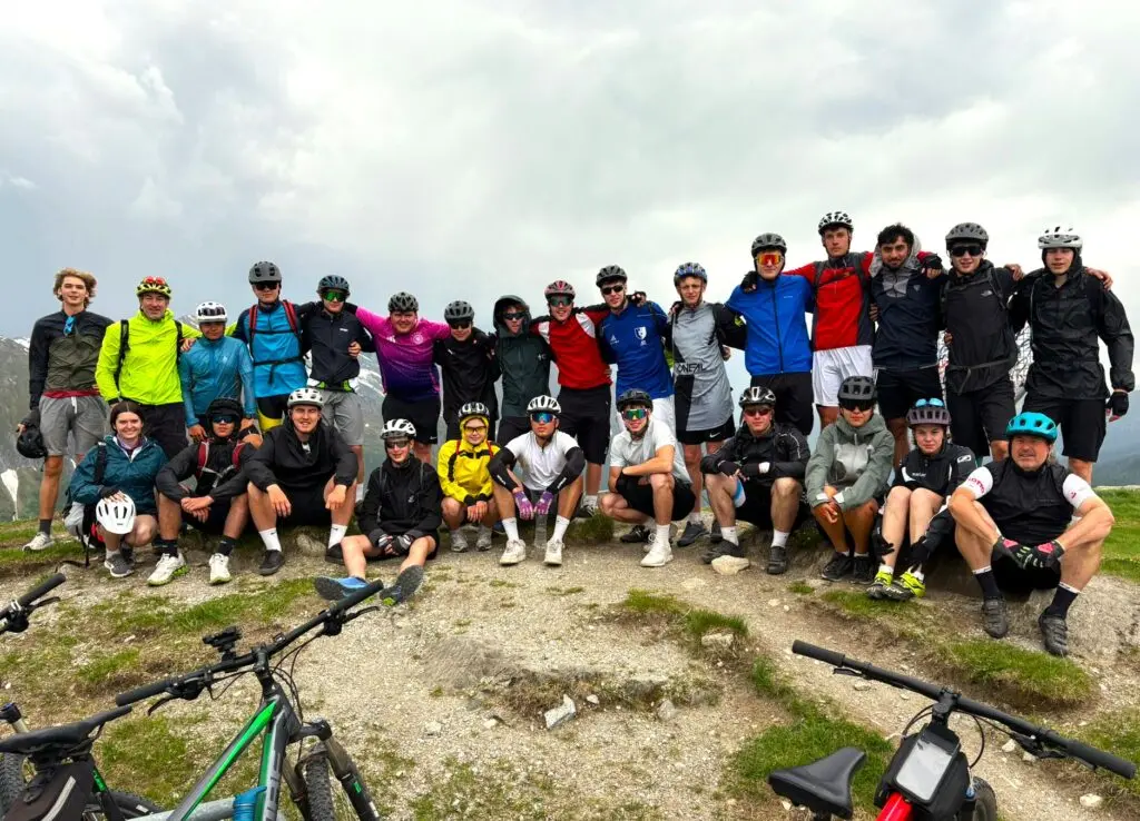 Gruppe Jugendlicher mit Fahrrädern und Helmen auf einem Berggipfel unter bewölktem Himmel
