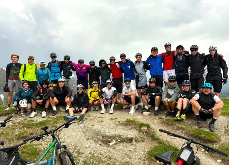 Gruppe Jugendlicher mit Fahrrädern und Helmen auf einem Berggipfel unter bewölktem Himmel