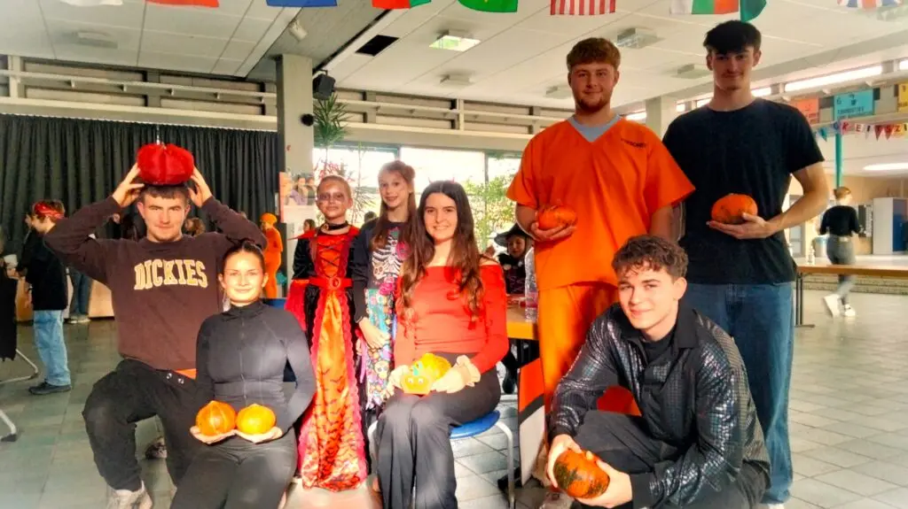 Schülerinnen und Schüler in Halloween-Kostümen posieren mit Kürbissen in der Pausenhalle