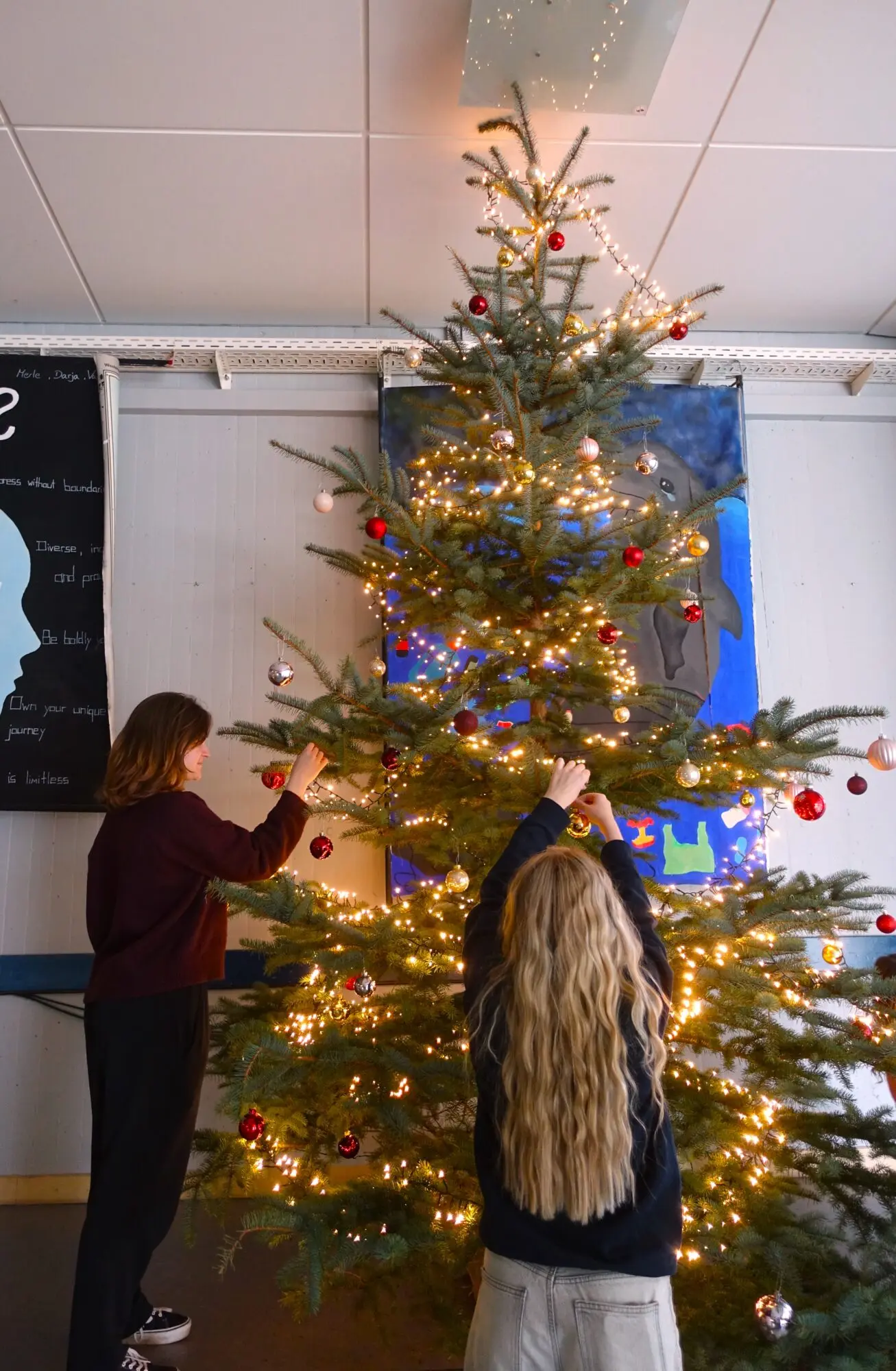 Schülerinnen schmücken einen beleuchteten Weihnachtsbaum in der Schule