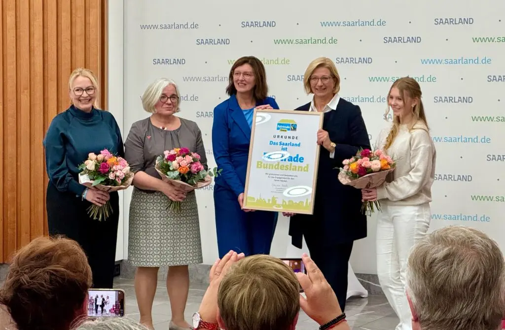 Frauen mit Blumensträußen und einer Urkunde bei einer Ehrung auf einer Bühne vor Publikum