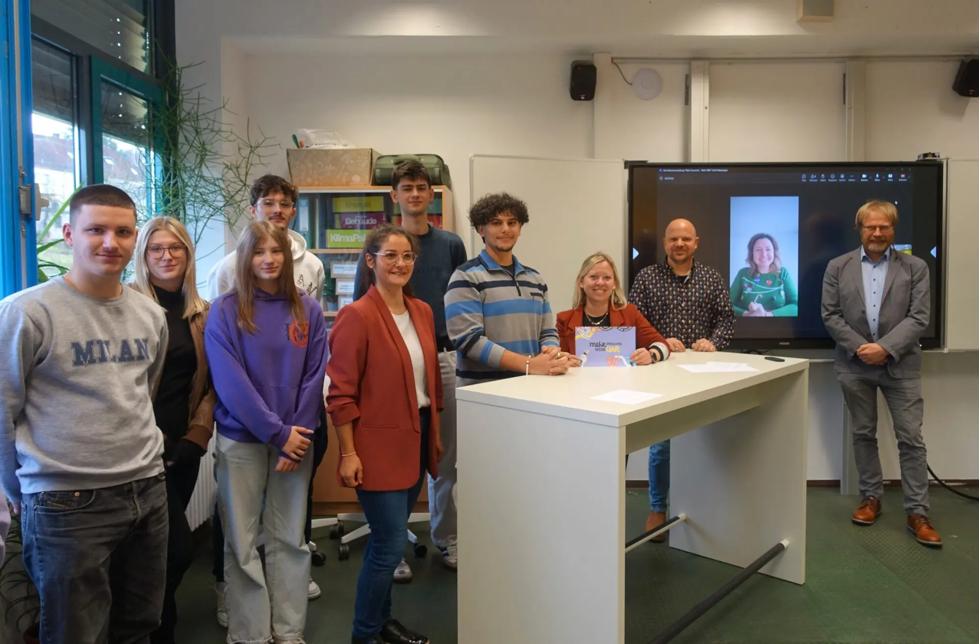 Gruppe von Schülerinnen, Schülern und Erwachsenen im Klassenraum vor einem großen Bildschirm