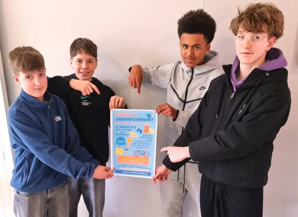 Vier Jungen präsentieren lachend ein blaues Plakat zum Kinder- und Jugendflohmarkt