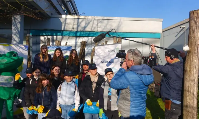 Schülergruppe mit Müllsäcken und einer grünen Maskottchenfigur vor dem Schulgebäude