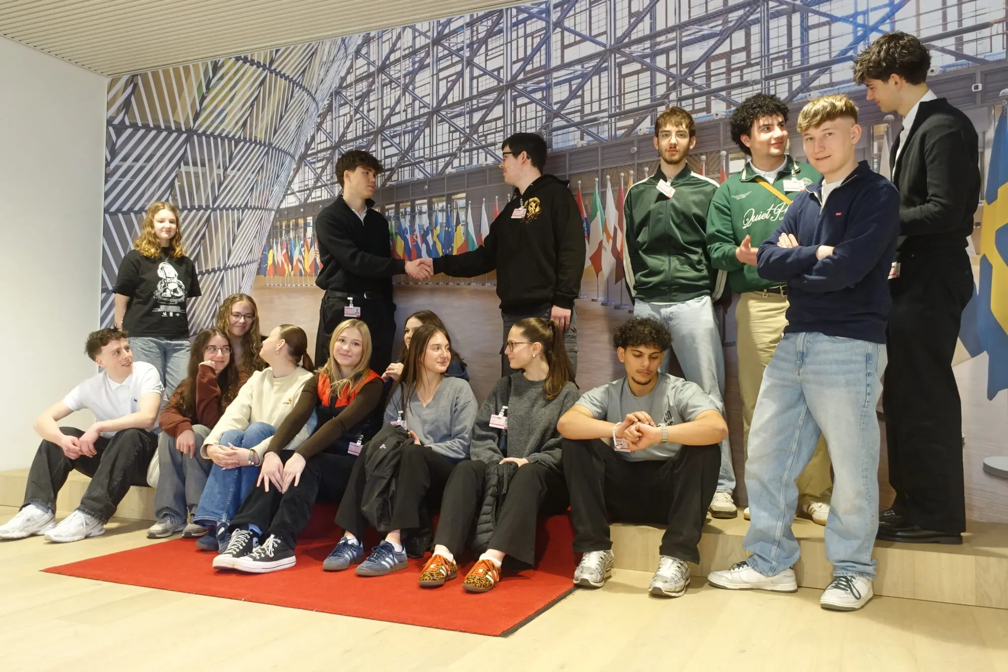 Schülerinnen und Schüler sitzen und stehen in einer Reihe auf einer Bank in einem modernen EU-Gebäude