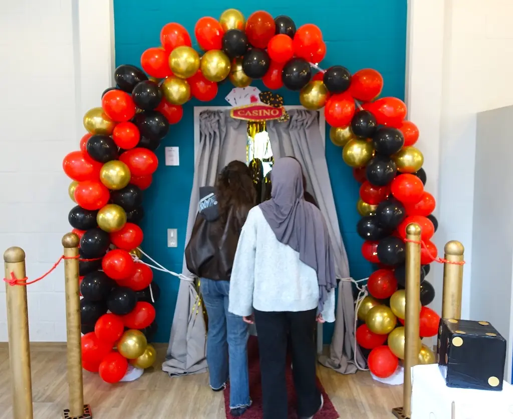 Fotobox mit Ballonbogen in Rot, Schwarz und Gold, davor stehen zwei Personen