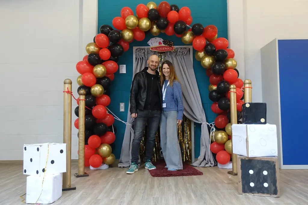 Zwei Jugendliche posieren unter einem Ballonbogen an einer Fotowand mit Würfeldeko